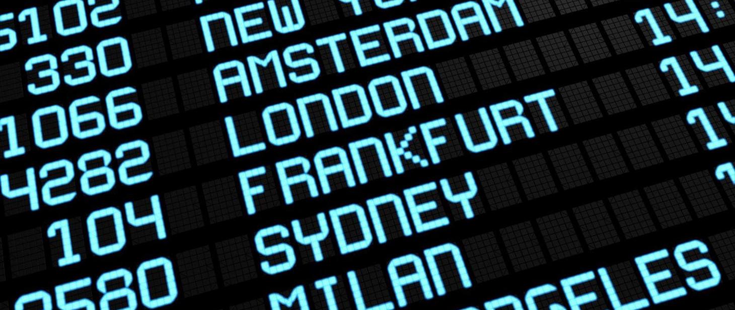 Tablica na lotnisku z nazwami miast: Amsterdam, Londyn, Frankfurt, Sydney